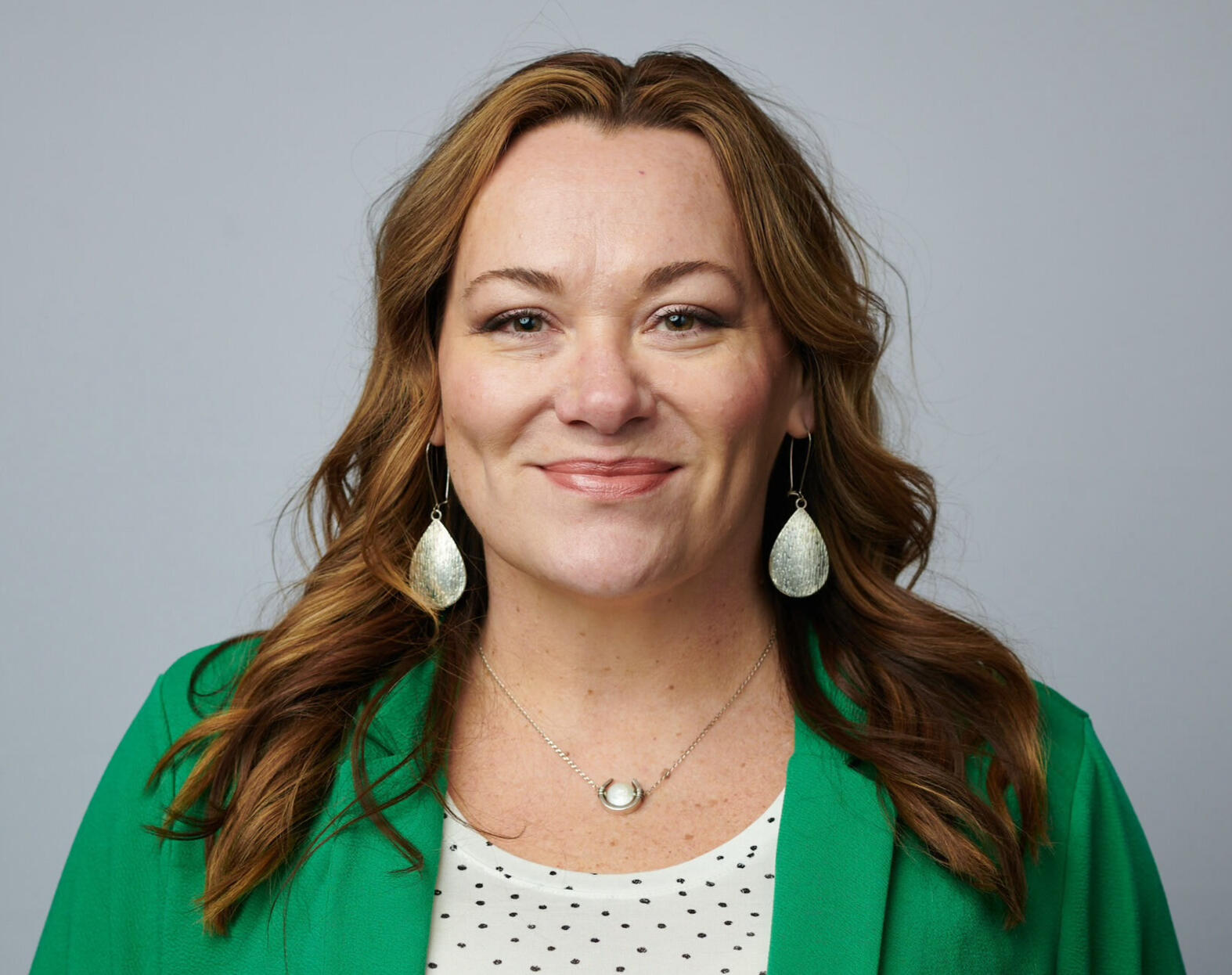 photograph of white woman with long brown hair, wearing a green blazer